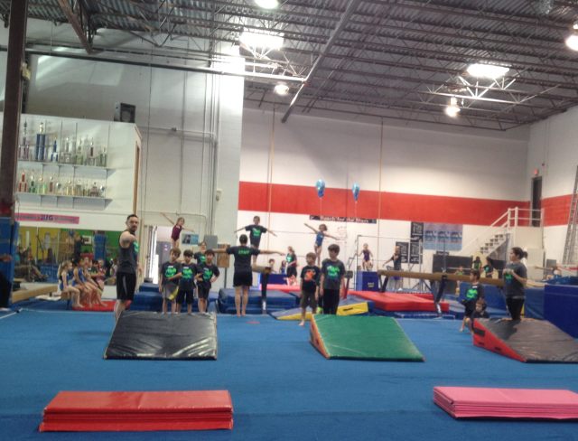 A dismal old factory, now filled with bouncing children. Leo is in the center in the black and orange shirt